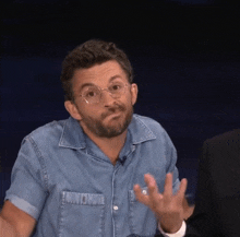 a man wearing glasses and a denim shirt is making a face
