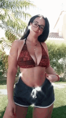 a woman in a bikini top and shorts is standing in a garden .