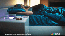a woman is sleeping in a bed with a nbc logo on the bottom