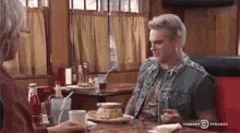a man and a woman are sitting at a table in a diner talking to each other .