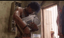 a man is holding a boombox in his hands in a room next to a window .