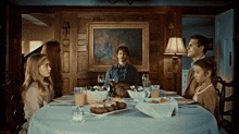 a family sits at a table with plates of food in front of a painting