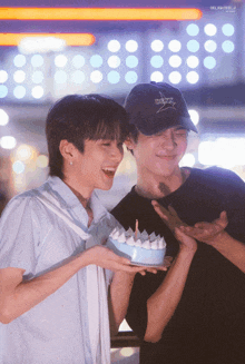 a man wearing a hat that says ' x-box ' on it holds a cake