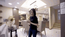 a woman in a black shirt is standing in a room with a dining table and chairs