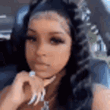 a woman with long hair is sitting in a car with her hand on her chin .
