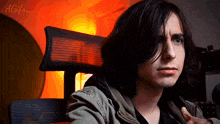 a young man with long dark hair is sitting in a chair and looking at the camera with a gif written in the corner