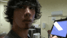 a man with curly hair holds a tablet in front of his face with the letter d visible in the corner