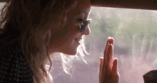 a woman wearing sunglasses is looking out of a car window and touching her hand to the glass .
