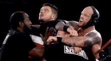 two wrestlers are fighting in a ring while a referee looks on .