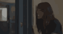 a woman is standing in front of a blue door and looking through it .