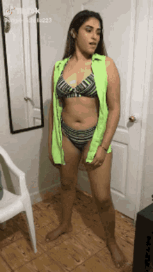 a woman in a bikini is standing in front of a mirror and a chair .