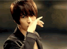 a young man in a black jacket is covering his face with his hand