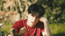 a young man wearing a red shirt is sitting outside