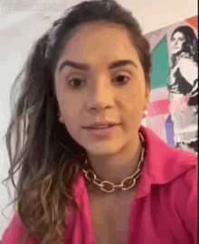 a woman is wearing a pink shirt and a gold necklace .