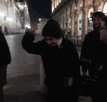 a man wearing a black hat and a black jacket is giving the middle finger