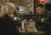 a man and a woman are sitting at a table with a bag of food
