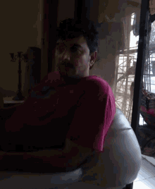a man in a pink shirt is sitting in a chair in front of a window