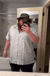 a man in a hat takes a picture of himself in a bathroom mirror