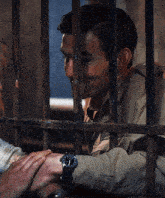 a man in a jail cell holds another man 's hand while wearing a watch
