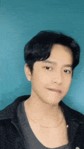 a young man wearing a black jacket and a gold chain around his neck is looking at the camera .
