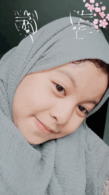 a girl wearing a gray scarf and a hijab smiles at the camera