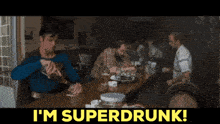 a man in a superman costume sits at a table with the words i 'm superdrunk below him