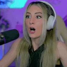 a woman is wearing headphones and making a surprised face while sitting in front of a microphone .