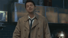 a man wearing a trench coat and tie stands in a kitchen