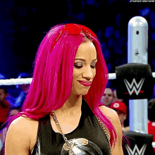 a woman with bright pink hair is standing in a wrestling ring wearing sunglasses .
