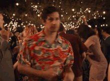 a man in a hawaiian shirt is dancing in a crowd of people .