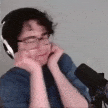 a man wearing headphones and glasses is sitting in front of a microphone and making a funny face .