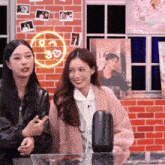 two women are standing next to each other in front of a brick wall with a neon sign that says 30