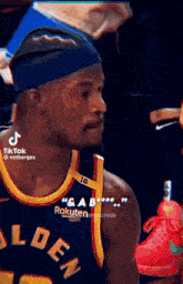 a basketball player wearing a headband and a golden state warriors jersey is holding a red shoe .