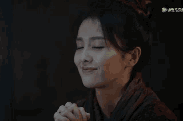 a close up of a woman 's face with her hands folded in prayer .
