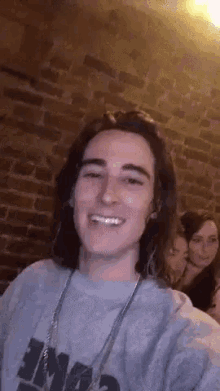 a young man with long hair is smiling for the camera while wearing a gray sweatshirt with the word mad on it .