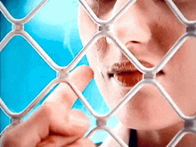a woman 's face is behind a chain link fence with her finger in her mouth