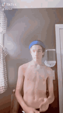 a shirtless boy wearing a blue headband is standing in front of a mirror .