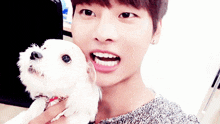 a young man is holding a small white dog