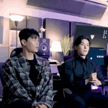 a man in a plaid shirt is sitting next to another man in a black shirt
