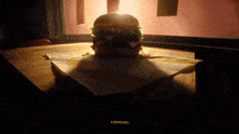 a hamburger is sitting on a napkin on a wooden table with a light shining on it and the word mcdonalds visible