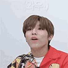 a young man in a red jacket is making a surprised face and looking up .