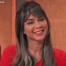 a woman in a red shirt is smiling and making a funny face with her hands in the air .