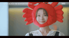 a woman wearing a red crab hat with sbs written on the bottom right
