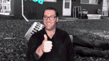 a man with glasses is giving a thumbs up in front of a building