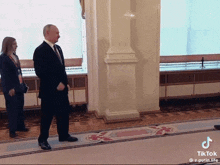 a man in a suit and tie is standing in a hallway with a woman standing behind him ..
