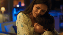 a woman is hugging a young boy who is wearing a blue shirt with flowers on it