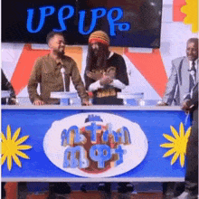a group of people are sitting at a table in front of a sign that says upupp .