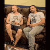 two men sitting on a couch one wearing a t-shirt that says rejox