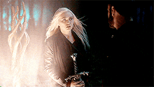 a man and a woman are standing next to each other in a dark forest .