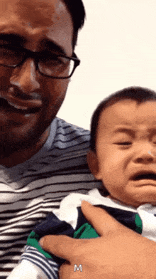 a man is holding a baby who is crying and the letter m is above him